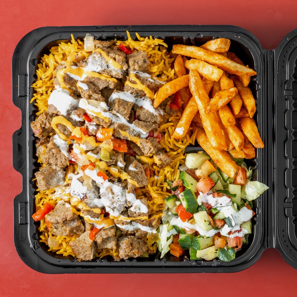 Takeout container filled with seasoned rice, sliced gyro meat, fries, salad, and drizzled white and orange sauces.