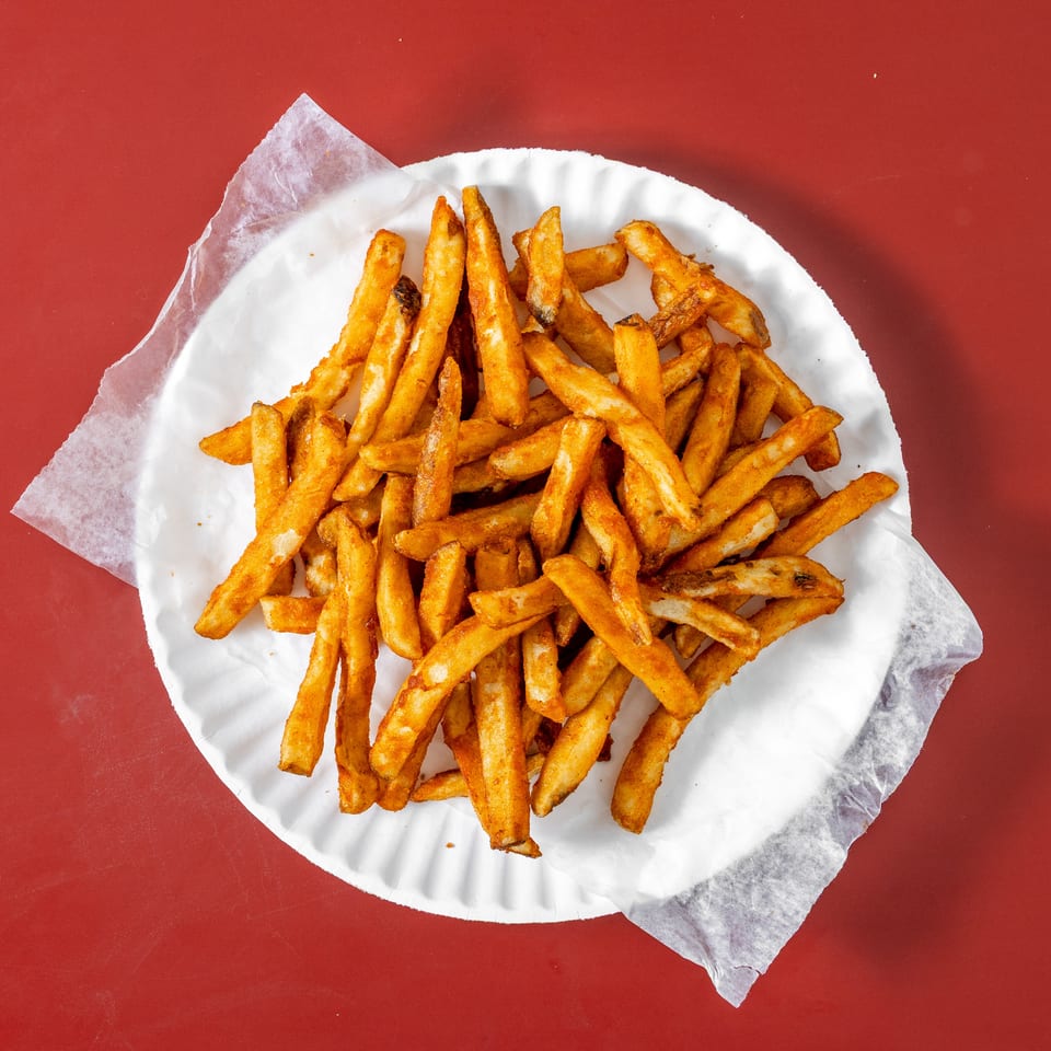 Pile of golden French fries served on a white paper plate over a red tabletop.