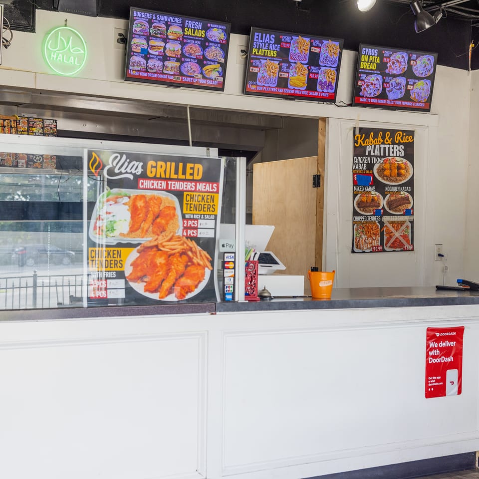 Elias Halal restaurant counter displaying menu boards for burgers, gyros, salads, rice platters, kababs, and chicken tenders.