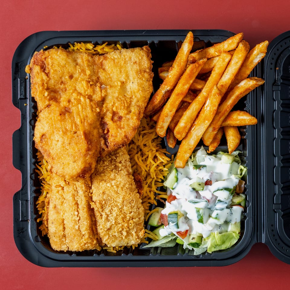 Open black takeout container filled with fried fish, seasoned rice, French fries, and creamy cucumber salad.