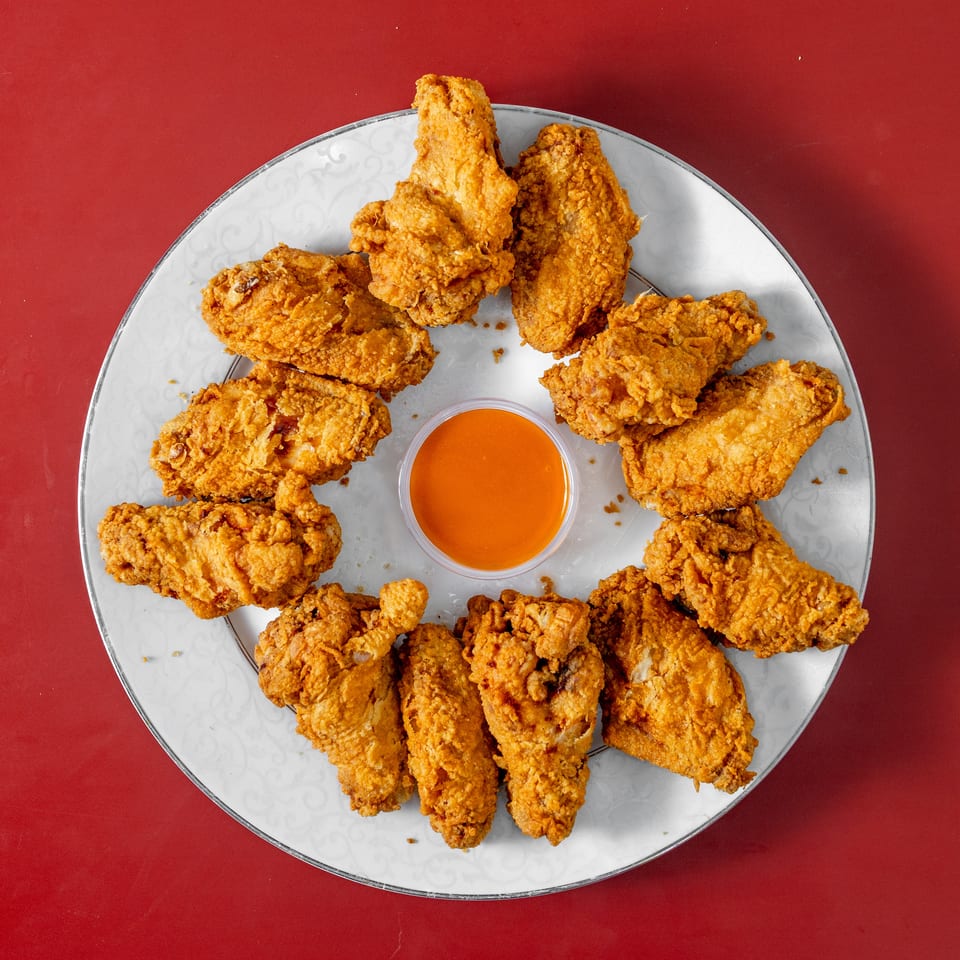 Plate of golden fried chicken pieces arranged around a bowl of orange dipping sauce on a red tabletop.
