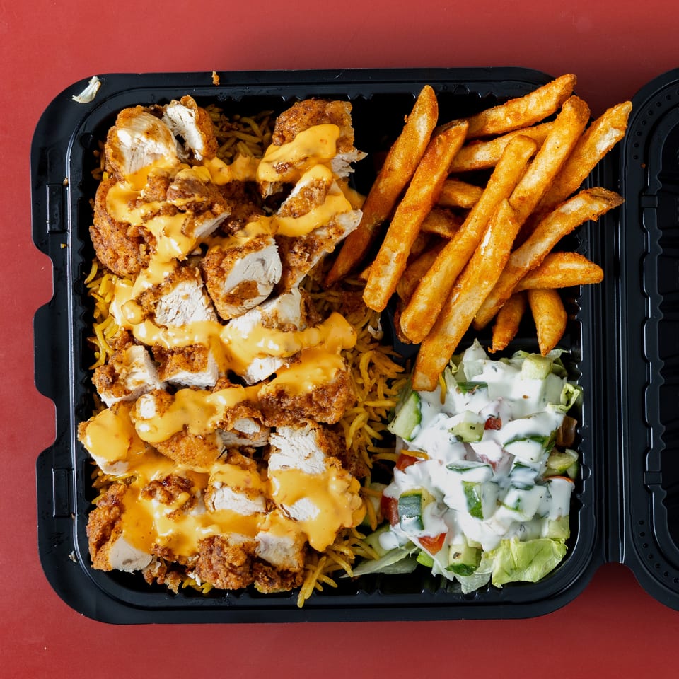 Takeout tray with crispy chicken, cheese sauce, seasoned rice, French fries, and creamy cucumber salad.