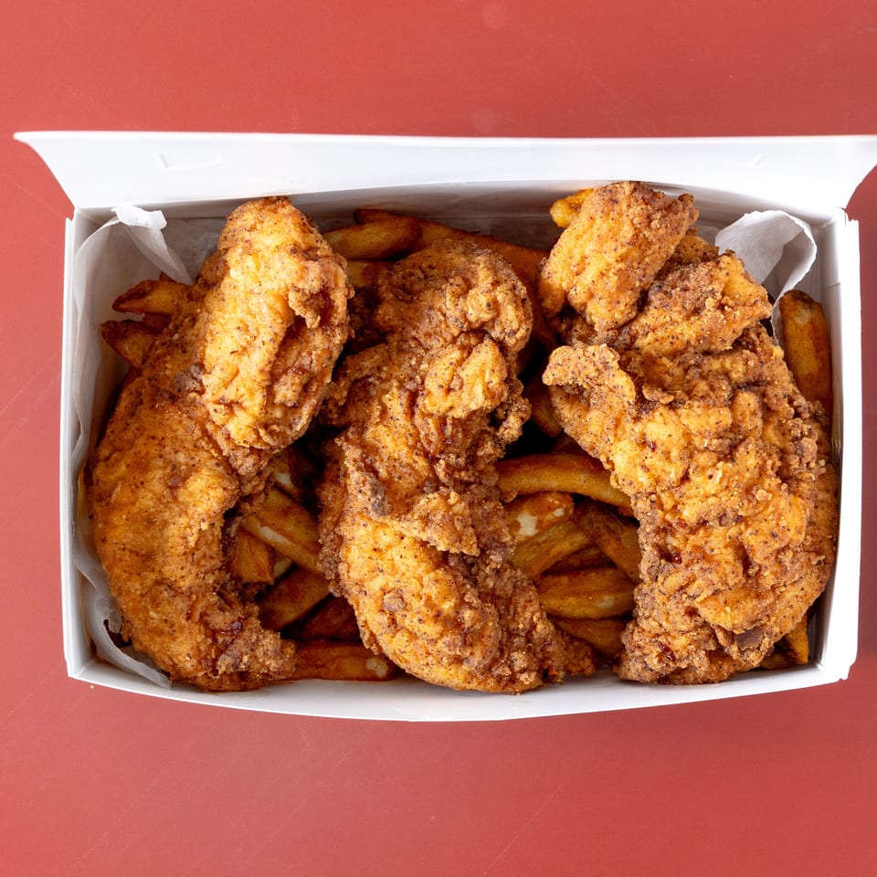 Open takeout box filled with crispy fried chicken pieces and golden fries on a red surface.