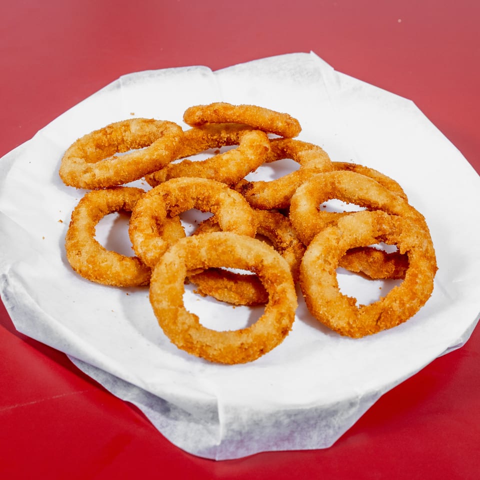 Crispy golden-breaded onion rings piled on white paper over a red table.