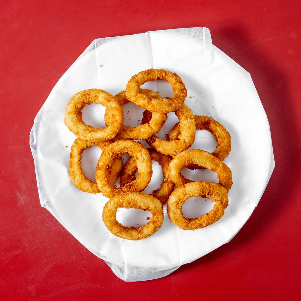 Golden-brown breaded onion rings piled on white paper atop a bright red surface.