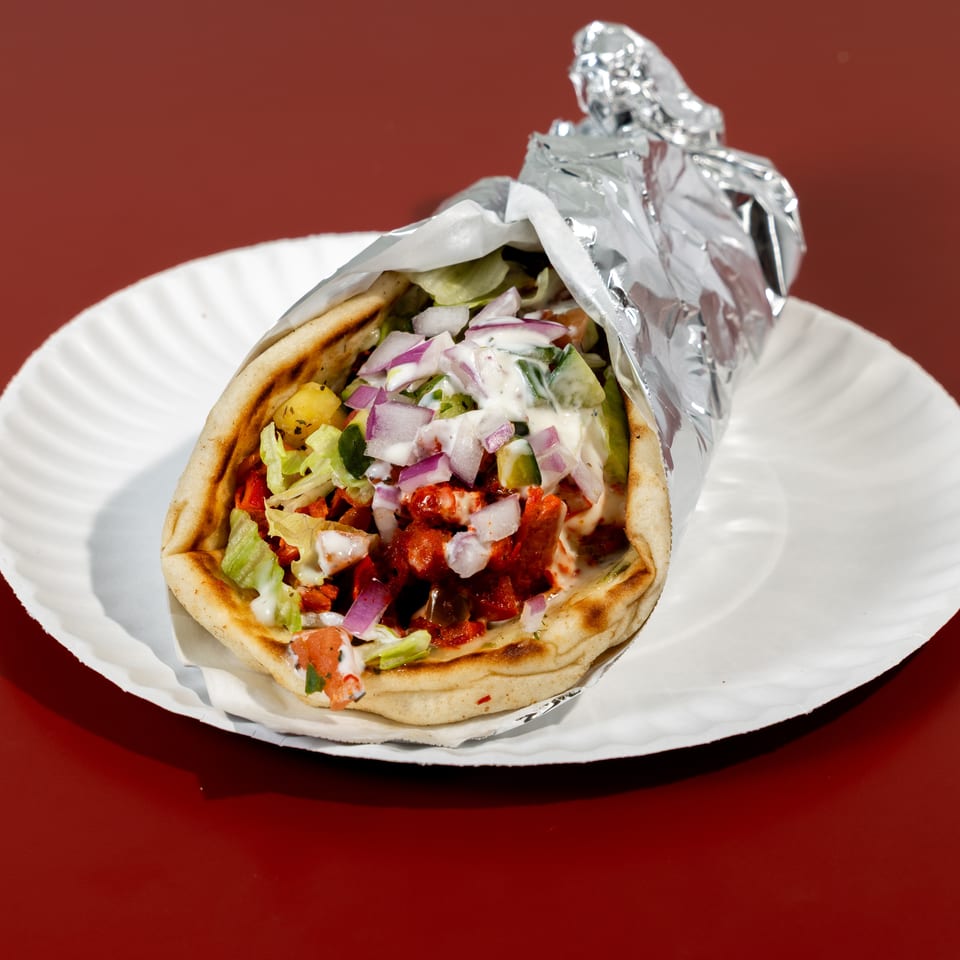 Gyro pita stuffed with seasoned meat, lettuce, tomatoes, red onions, cucumbers, and creamy sauce on a paper plate.