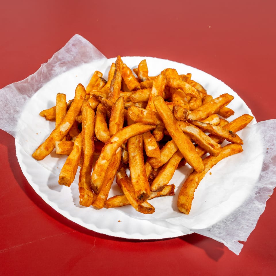 Pile of golden French fries served on white paper atop a red table.