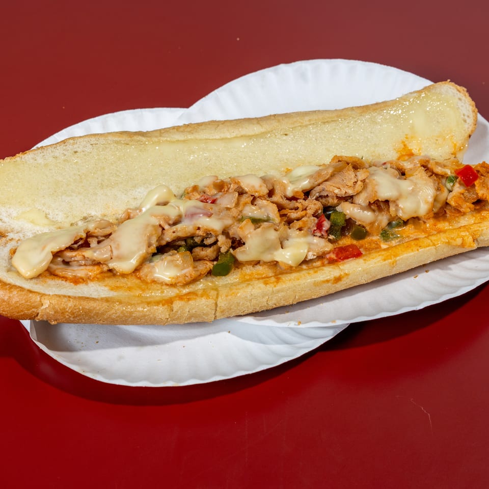 Loaded toasted sub sandwich with sliced meat, melted cheese, peppers, and onions on a white paper plate.