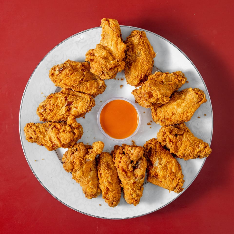 Overhead view of a platter of crispy fried chicken pieces surrounding a bowl of orange dipping sauce on a red table.
