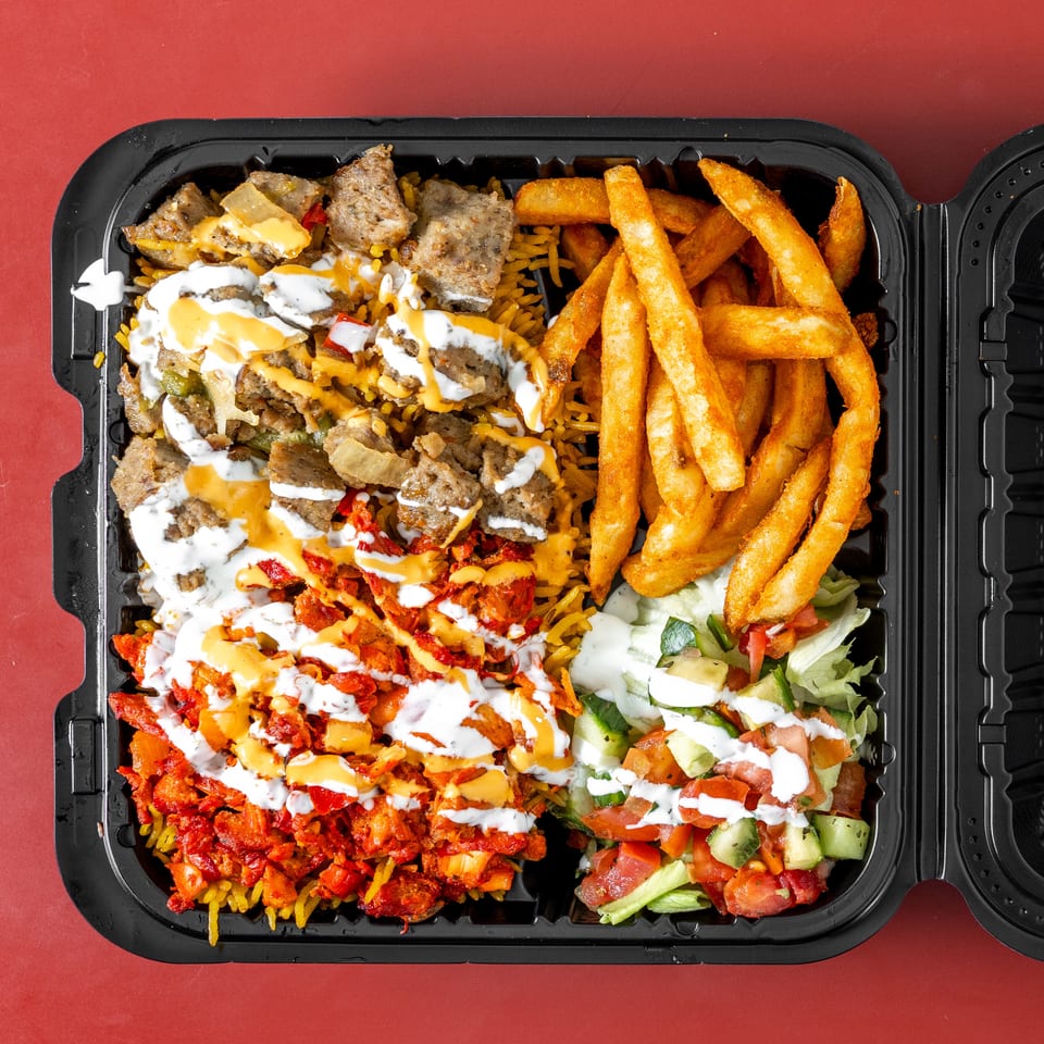 Open takeout container filled with seasoned rice, gyro meat, chicken, fries, salad, and creamy sauces.